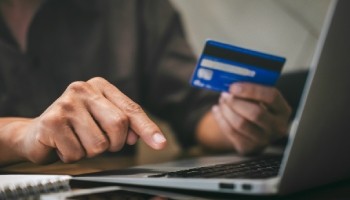 a man is holding a credit card while using a laptop