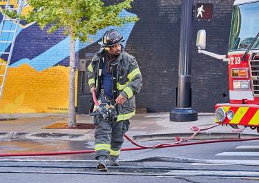 firefighter carrying a water hose across a street