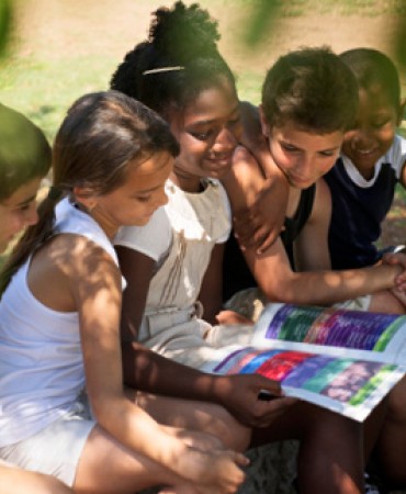 five children sitting closely together reading a book