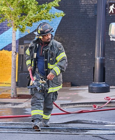 firefighter carrying a water hose across a street